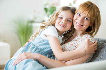 Mother and daughter sitting on couch, cuddling - WESTF021499