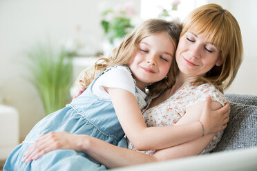 Mother and daughter sitting on couch, cuddling - WESTF021500