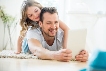 Vater und Tochter liegen auf dem Boden und benutzen ein digitales Tablet - WESTF021524