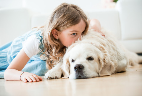 Kleines Mädchen kuschelt mit ihrem Hund, auf dem Boden liegend, lizenzfreies Stockfoto