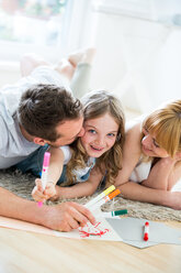 Kleines Mädchen liegt mit seinen Eltern auf dem Boden und zeichnet mit Filzstiften - WESTF021539