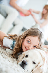 Little girl cuddling with her dog, lying on floor, parents in background - WESTF021547