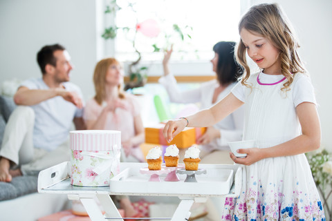 Mädchen garniert Tassenkuchen, im Hintergrund feiert die Familie, lizenzfreies Stockfoto