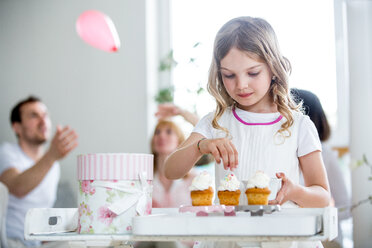 Mädchen garniert Tassenkuchen, im Hintergrund feiert die Familie - WESTF021569
