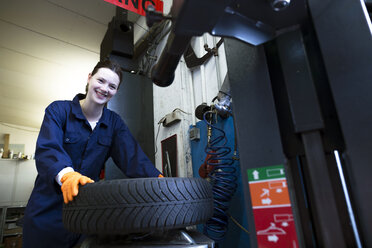 Young woman working in repair garage taking car tire - SGF001803