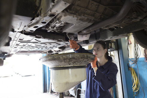 Young woman working in repair garage, changing oil - SGF001805