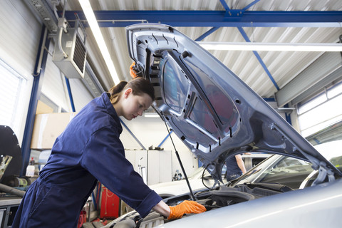 Junge Frau arbeitet in einer Reparaturwerkstatt und überprüft den Motor, lizenzfreies Stockfoto