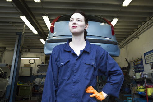 Junge Frau bei der Arbeit in einer Reparaturwerkstatt, vor einer Hebebühne stehend - SGF001810