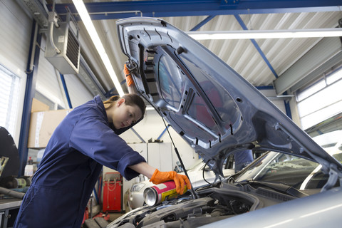 Junge Frau arbeitet in einer Reparaturwerkstatt und überprüft den Motor, lizenzfreies Stockfoto