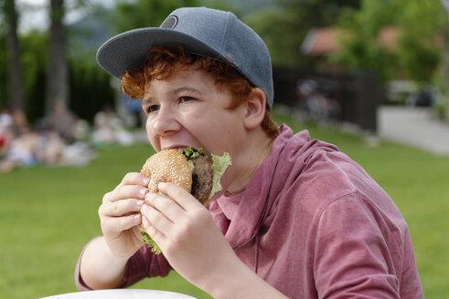 Jugendlicher mit Baseballmütze beim Essen eines Hamburgers - LBF001153