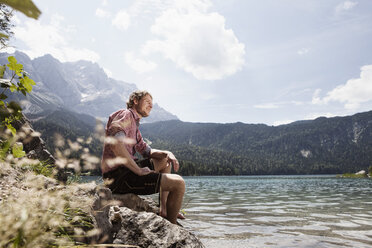 Deutschland, Bayern, Eibsee, lächelnder Mann in Lederhosen am Seeufer sitzend - RBF003007