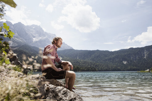 Germany, Bavaria, Eibsee, smiling man in lederhosen sitting on lakeshore - RBF003007