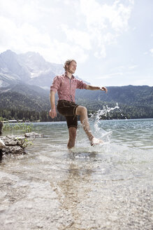 Germany, Bavaria, Eibsee, happy man in lederhosen splashing in water - RBF003010