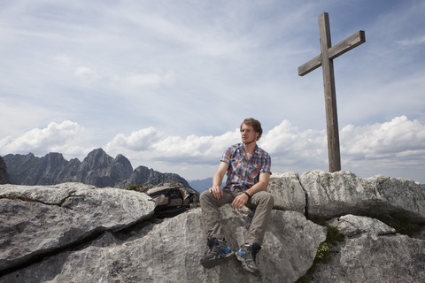 Deutschland, Bayern, Osterfelderkopf, Mann sitzt am Gipfelkreuz, lizenzfreies Stockfoto