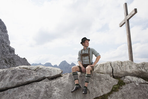 Germany, Bavaria, Osterfelderkopf, man in traditional clothes sitting at summit cross - RBF003023