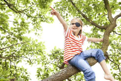 Mädchen als Pirat verkleidet sitzt auf einem Baum und zeigt mit dem Finger - MFRF000282