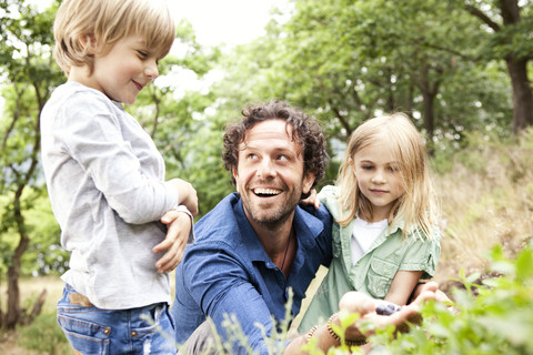 Vater mit zwei Kindern beim Sammeln von Heidelbeeren in der Natur, lizenzfreies Stockfoto