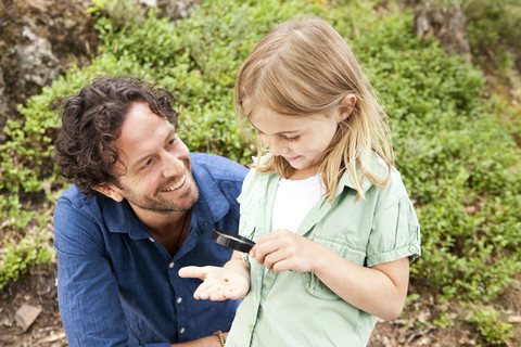 Mädchen mit Vater schaut durch ein Vergrößerungsglas, lizenzfreies Stockfoto