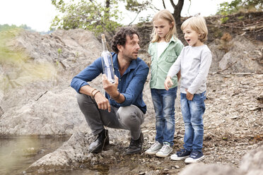 Father with two children with message in a bottle at lakeshore - MFRF000332