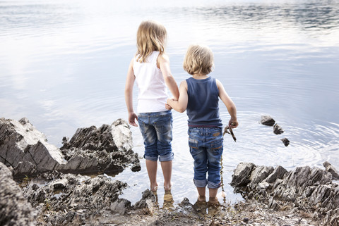 Junge und Mädchen stehen Hand in Hand am Seeufer, lizenzfreies Stockfoto