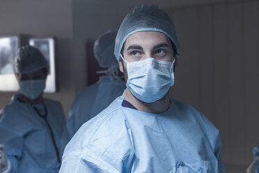 Portrait of surgeon wearing mask with team in background - ZEF007381