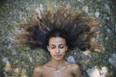Porträt einer auf einem Felsen liegenden jungen Frau mit zerzaustem Haar und geschlossenen Augen - RAEF000248