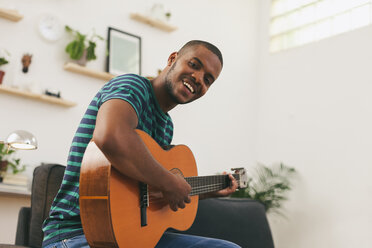 Portrait of smiling man playing guitar at home - EBSF000847