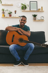 Portrait of smiling man sittining on a couch with guitar - EBSF000850
