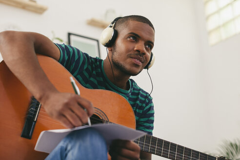 Mann mit Gitarre hört Musik mit Kopfhörern und schreibt etwas auf - EBSF000854