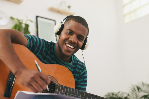 Porträt eines lächelnden Mannes mit Gitarre, der mit Kopfhörern Musik hört - EBSF000855