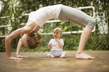 Frau macht Yoga-Übungen, während ihr Baby sie beobachtet - ABF000630