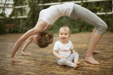 Frau macht Yoga-Übungen, während ihr Baby sie beobachtet - ABF000631