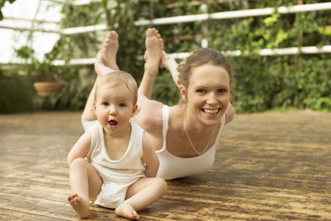 Porträt eines Babys, das vor der Mutter sitzt, die Yogaübungen macht, lizenzfreies Stockfoto