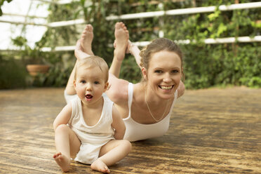 Porträt eines Babys, das vor der Mutter sitzt, die Yogaübungen macht - ABF000637