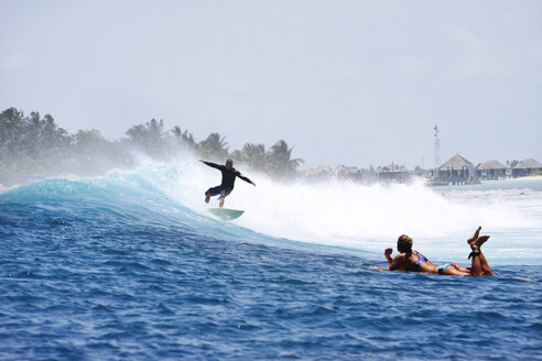 Maledives, South Male Atoll, man surfing while woman lying on her surfboard watching him - FAF000067
