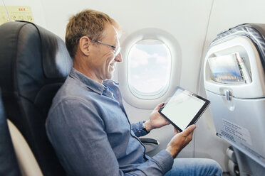 Älterer Mann sitzt in einem Flugzeug und schaut auf sein digitales Tablet - MFF001980