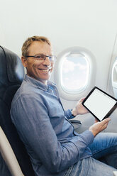 Porträt eines lächelnden Mannes, der in einem Flugzeug sitzt und ein digitales Tablet hält - MFF001981