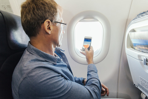 Mann fotografiert mit seinem Handy aus dem Fenster, während er in einem Flugzeug fliegt, lizenzfreies Stockfoto