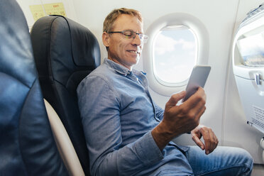 Älterer Mann sitzt in einem Flugzeug und schaut auf sein Smartphone - MFF001983