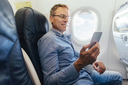 Älterer Mann sitzt in einem Flugzeug und schaut auf sein Smartphone - MFF001983