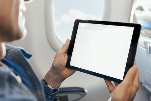 Mann sitzt in einem Flugzeug und hält ein digitales Tablet - MFF001997