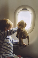 Little boy sitting on an airplane with his soft toy looking through window - MFF001989