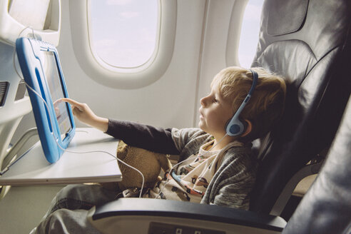 Kleiner Junge sitzt in einem Flugzeug und sieht sich etwas auf einem digitalen Tablet an - MFF001993