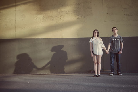 Teenage couple standing hand in hand in front of a wall stock photo