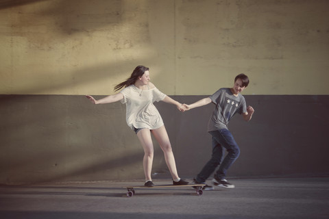 Teenager, der seine Freundin auf einem Longboard stehend zieht, lizenzfreies Stockfoto