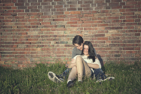 Teenage couple sitting on a meadow in front of a brick wall stock photo