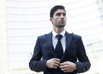 Portrait of young businessman buttoning his suit jacket - PASF000004