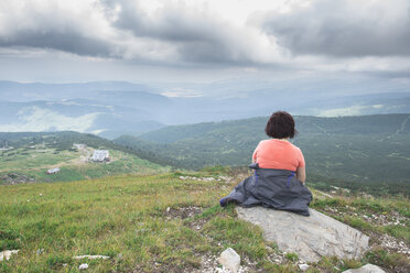 Bulgaria, Rila Mountains, back view of senior woman sitting on a rock looking at view - DEGF000490