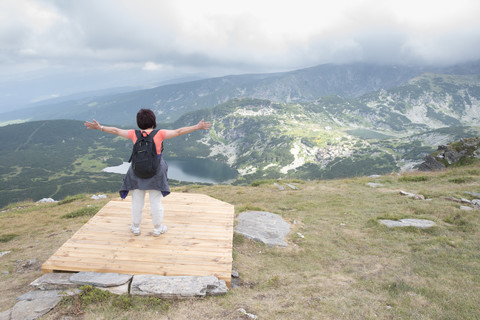 Bulgarien, Rila-Gebirge, Rückenansicht einer älteren Frau mit ausgestreckten Armen, die die Aussicht betrachtet, lizenzfreies Stockfoto