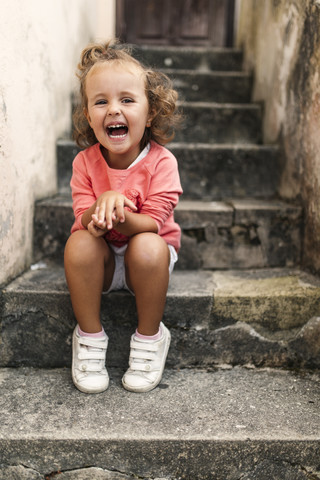 Porträt eines lachenden kleinen Mädchens, das auf einer Treppe sitzt, lizenzfreies Stockfoto